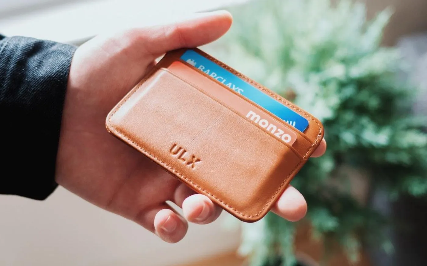 A person holding a small, brown leather wallet in their hand, showcasing its compact design and texture.