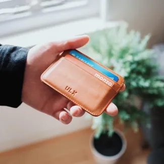 A person holding a small, brown leather wallet in their hand, showcasing its compact design and texture.