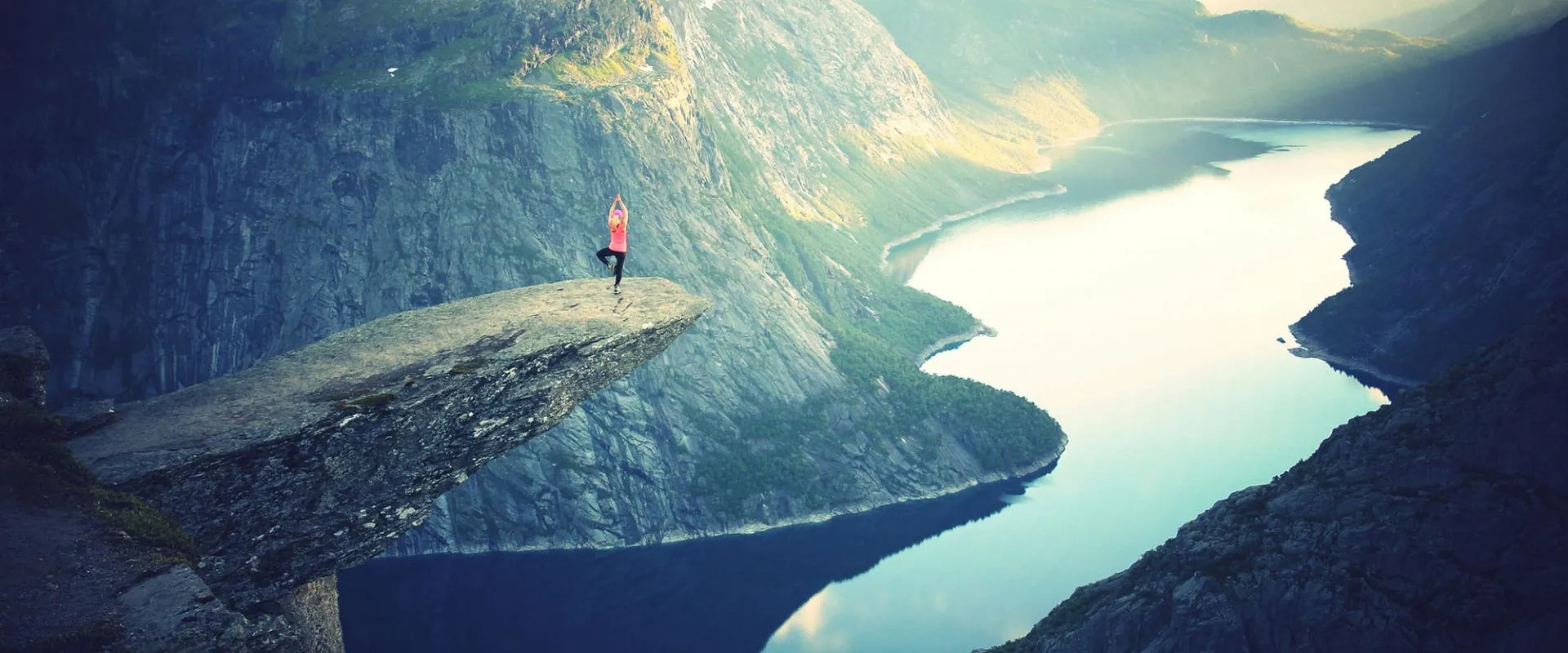 A person stands on a cliff, gazing at a winding river below, surrounded by lush greenery and a clear blue sky.