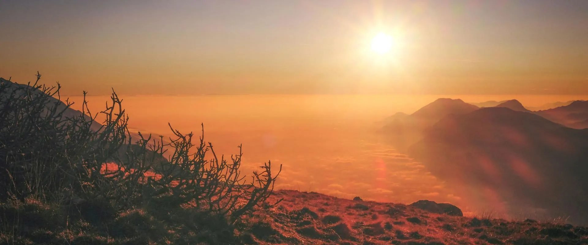 A vibrant sunset casts warm hues over a majestic mountain range, highlighting the peaks against the colorful sky.