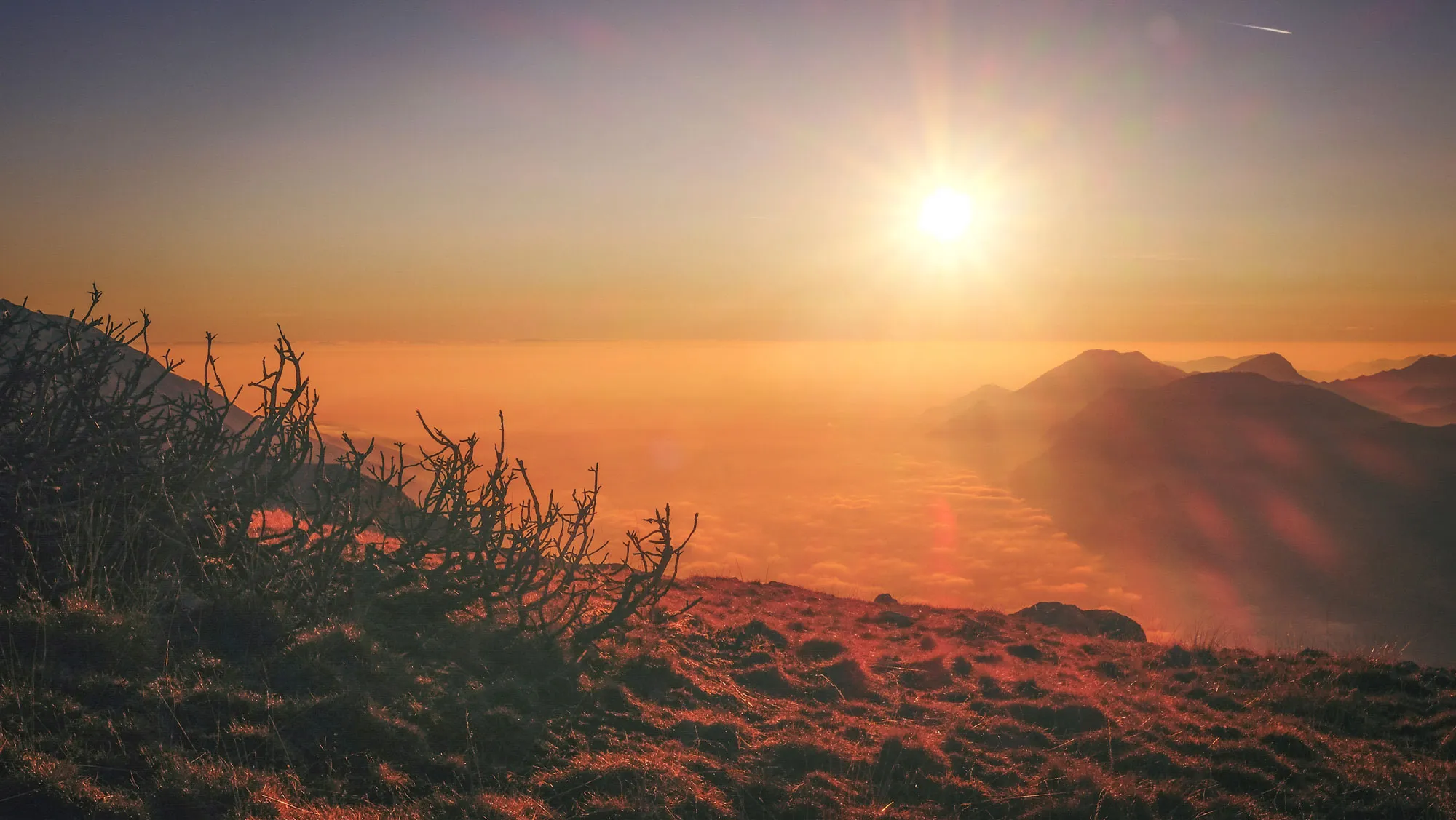 A vibrant sunrise breaks over a mountain range, filling the landscape with golden hues and soft morning light.