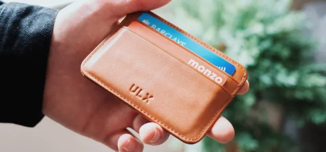 A person holding a small, brown leather wallet in their hand, showcasing its compact design and texture.